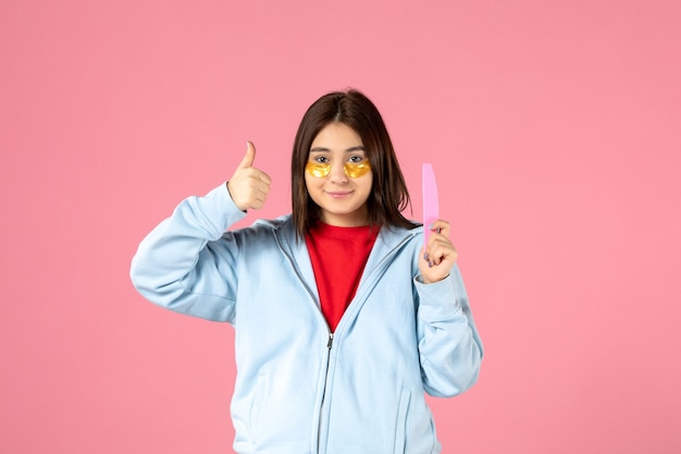 vue de face d'une jeune femme avec des cache-œil et une lime à ongles sur un mur rose