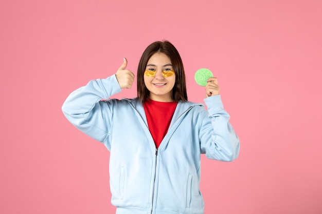 vue de face d'une jeune femme avec des cache-œil et une petite éponge sur un mur rose