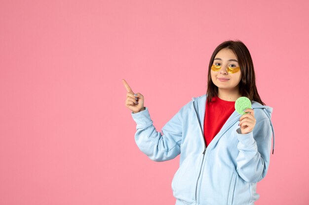 vue de face d'une jeune femme avec des cache-œil et une petite éponge de peau sur un mur rose