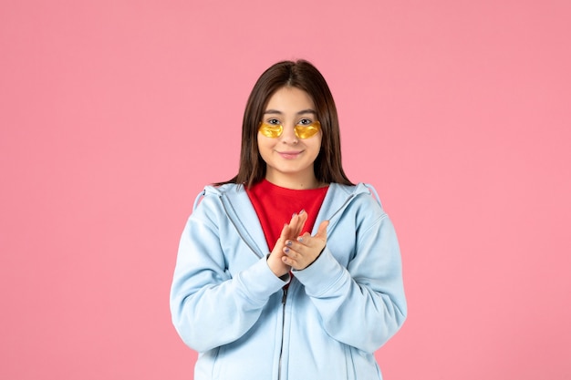 vue de face d'une jeune femme avec des cache-œil sous ses yeux applaudissant sur un mur rose