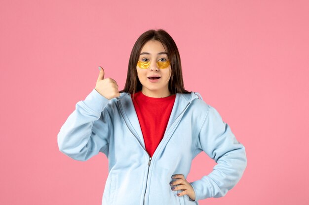 vue de face d'une jeune femme avec des cache-œil sous ses yeux sur un mur rose