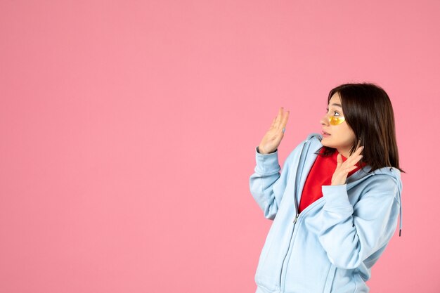 vue de face d'une jeune femme avec des cache-œil sous ses yeux sur un mur rose