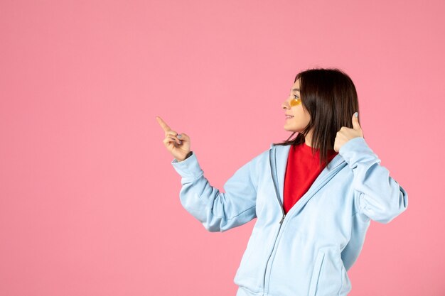 vue de face d'une jeune femme avec des cache-œil sous ses yeux sur un mur rose