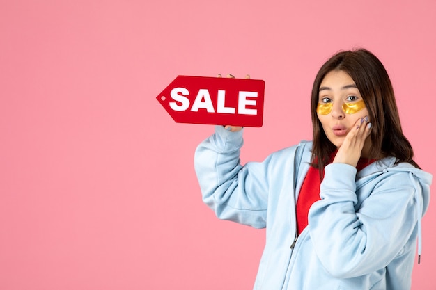 Photo gratuite vue de face d'une jeune femme avec des cache-œil tenant une bannière de vente rouge sur un mur rose