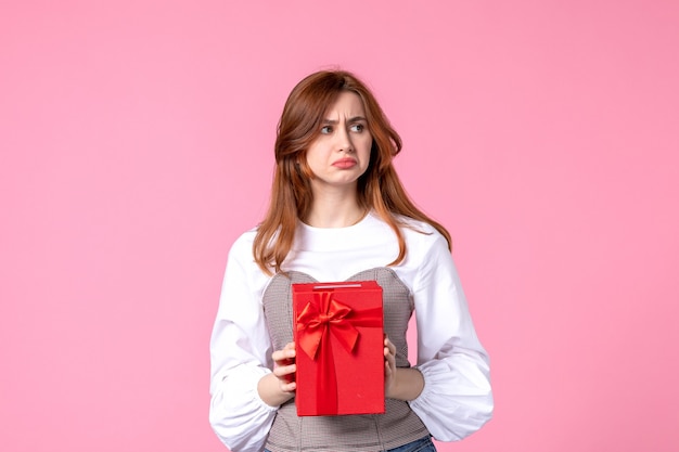 Vue de face jeune femme avec cadeau dans un emballage rouge sur fond rose mars cadeau sensuel horizontal femme de l'égalité de photo de parfum de cadeau