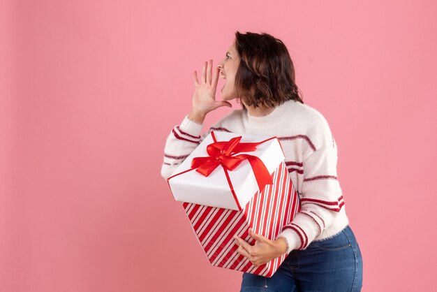 Vue de face de la jeune femme avec cadeau de Noël appelant sur mur rose