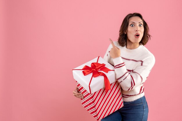 Photo gratuite vue de face de la jeune femme avec un cadeau de noël sur le mur rose