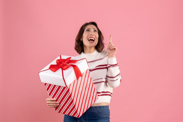 Vue de face de la jeune femme avec un cadeau de Noël sur le mur rose