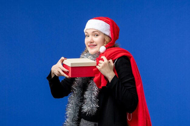 Vue de face d'une jeune femme avec un cadeau de vacances sur le mur bleu