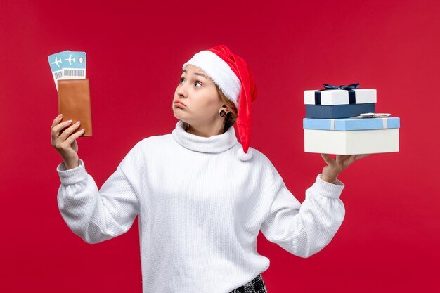 Vue de face jeune femme avec des cadeaux et des billets sur un bureau rouge