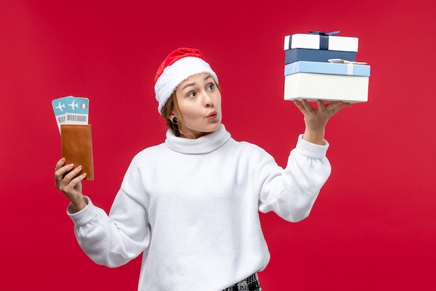 Vue de face jeune femme avec des cadeaux et des billets sur fond rouge