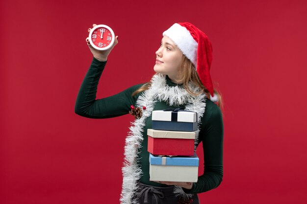 Vue de face jeune femme avec des cadeaux et horloge sur fond rouge