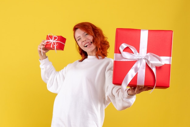 Vue de face de la jeune femme avec des cadeaux de Noël sur mur jaune