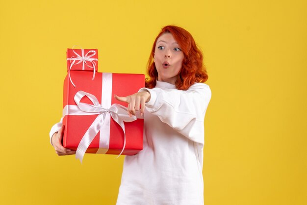 Vue de face de la jeune femme avec des cadeaux de Noël sur mur jaune