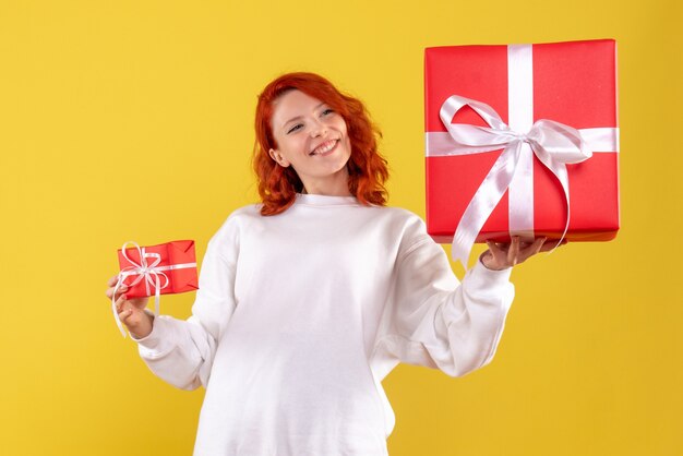 Vue de face de la jeune femme avec des cadeaux de Noël sur mur jaune