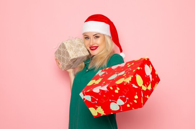 Vue de face d'une jeune femme avec des cadeaux de Noël sur le mur rose
