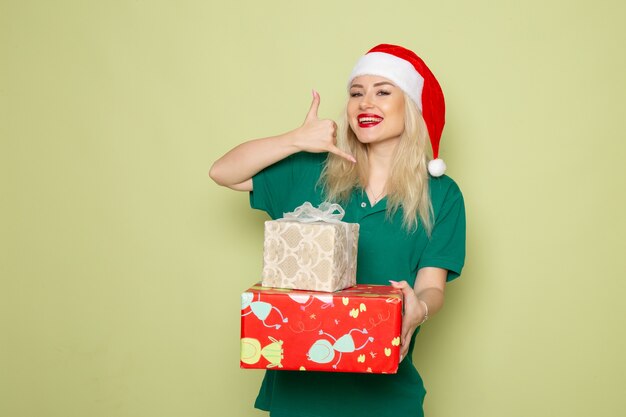 Vue de face d'une jeune femme avec des cadeaux de Noël sur un mur vert