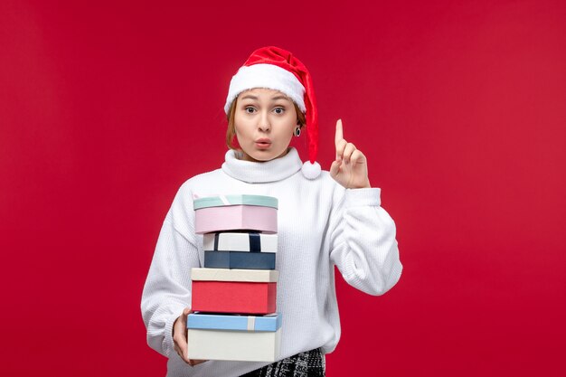 Vue de face jeune femme avec des cadeaux de nouvel an sur un bureau rouge