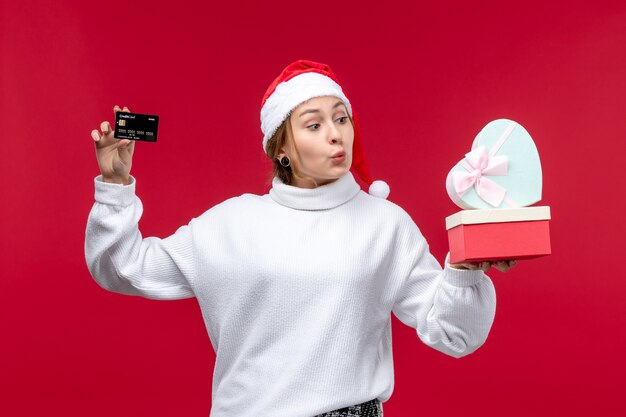 Vue de face jeune femme avec carte bancaire et cadeaux sur un bureau rouge