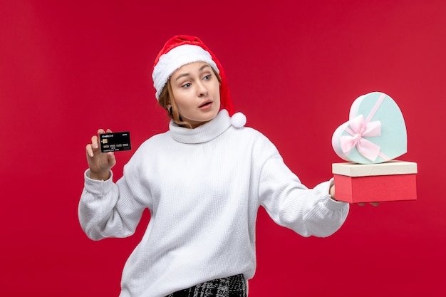 Vue de face jeune femme avec carte bancaire et cadeaux sur un bureau rouge