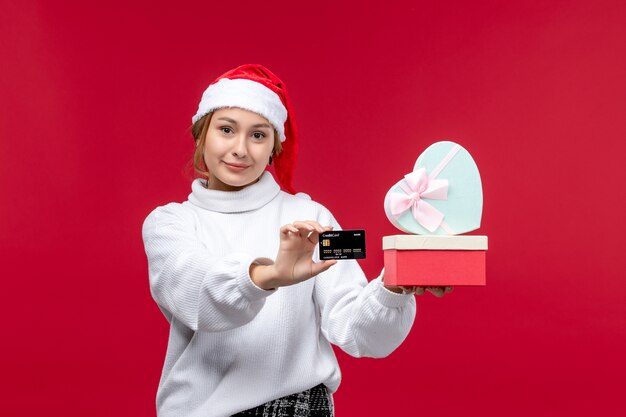 Vue de face jeune femme avec carte bancaire et cadeaux sur fond rouge