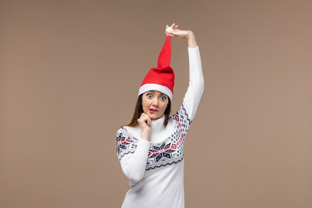 Vue de face jeune femme avec chapeau de Noël rouge sur le bureau brun émotions de vacances de Noël