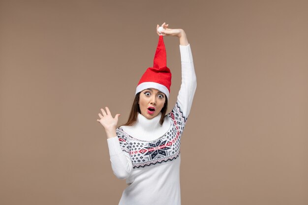 Vue de face jeune femme avec chapeau de Noël rouge sur le fond brun émotion de vacances de Noël