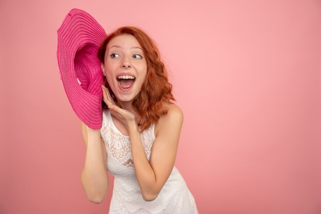 Vue de face de la jeune femme avec chapeau rose sur mur rose