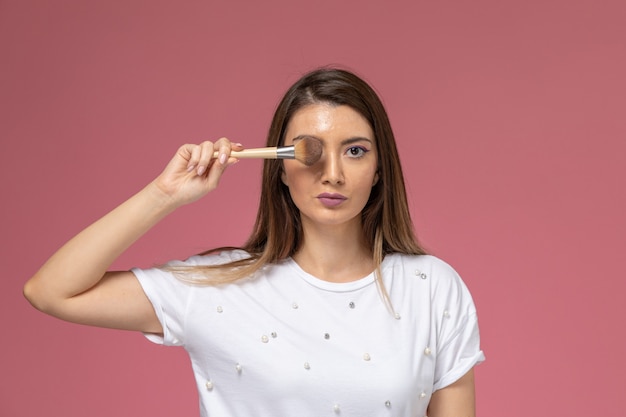 Vue de face jeune femme en chemise blanche couvrant ses yeux avec une brosse sur le mur rose modèle femme beauté