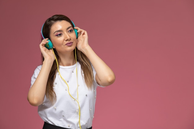 Vue de face jeune femme en chemise blanche, écouter de la musique sur le mur rose, modèle de pose de femme de couleur