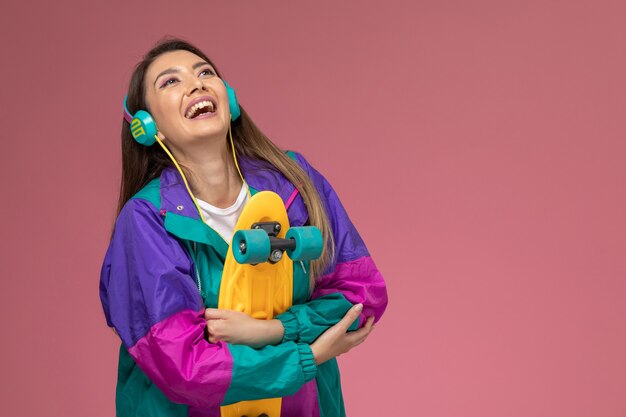 Vue de face jeune femme en chemise blanche manteau de couleur à écouter de la musique souriant sur mur rose, modèle de pose de femme de couleur