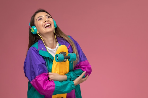 Vue de face jeune femme en chemise blanche manteau de couleur à écouter de la musique souriant sur mur rose, modèle de pose de femme de couleur