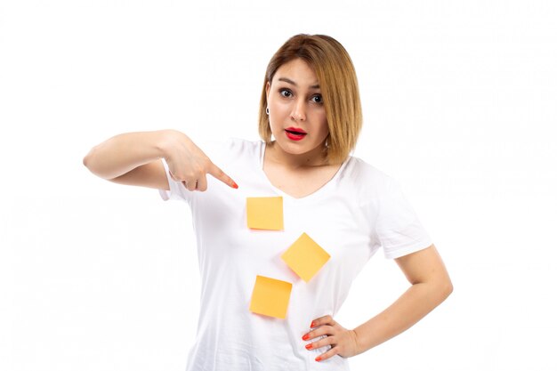 Une vue de face jeune femme en chemise blanche avec des notes orange posant sur le blanc