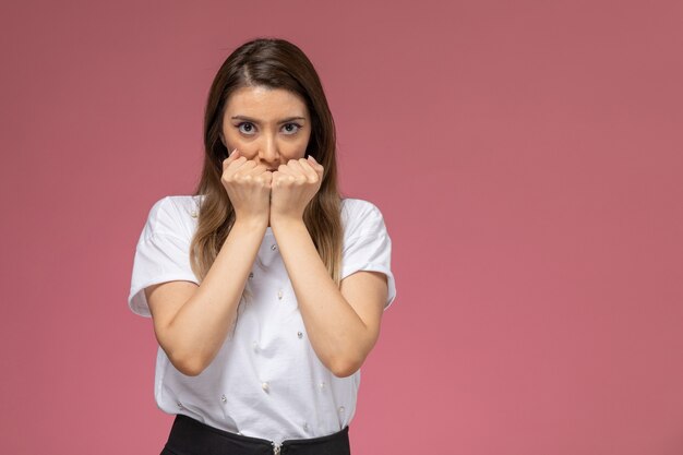 Vue de face jeune femme en chemise blanche avec les poings serrés sur le mur rose, modèle femme