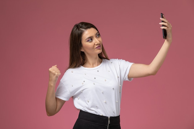 Vue de face jeune femme en chemise blanche prenant un selfie sur le mur rose, modèle femme pose