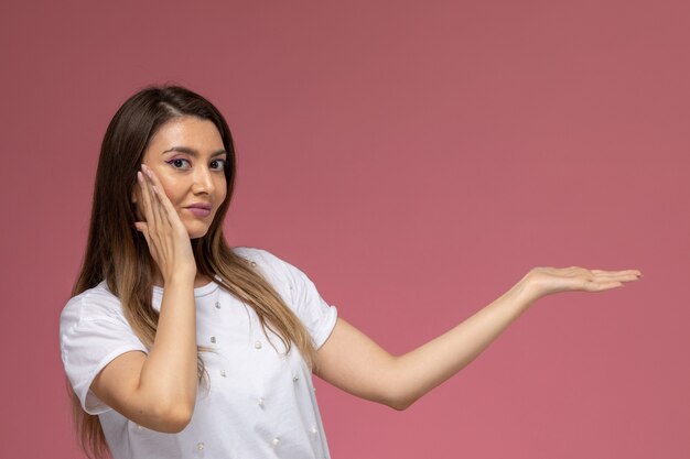 Vue de face jeune femme en chemise blanche souriant posant sur un mur rose, modèle de pose de femme de couleur