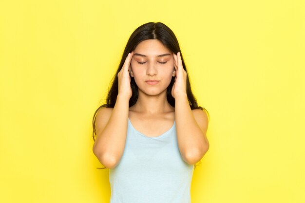 Une vue de face jeune femme en chemise bleue ayant un mal de tête sur le fond jaune fille pose modèle beauté jeune