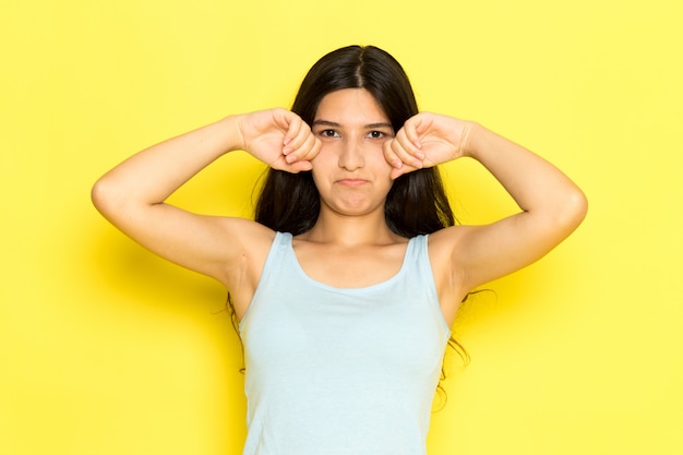 Une vue de face jeune femme en chemise bleue posant et faux pleurer sur le fond jaune fille pose modèle beauté jeune