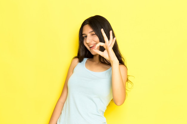 Une vue de face jeune femme en chemise bleue posant souriant et montrant bien signe