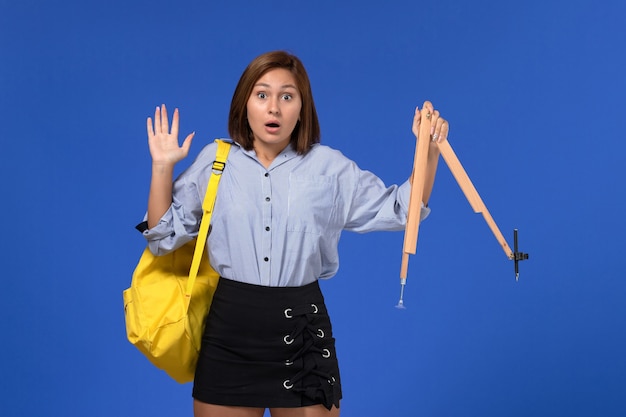 Vue de face de la jeune femme en chemise bleue tenant une figure en bois sur un mur bleu clair