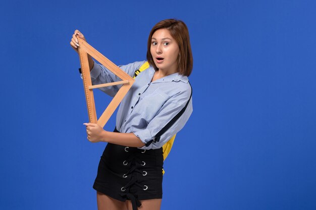 Photo gratuite vue de face de la jeune femme en chemise bleue tenant une forme de triangle en bois sur le mur bleu
