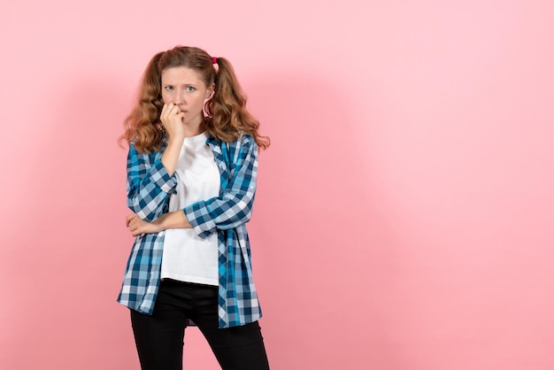 Vue de face jeune femme en chemise à carreaux bleu posant et pensant sur un mur rose kid girl jeunesse émotions modèle mode