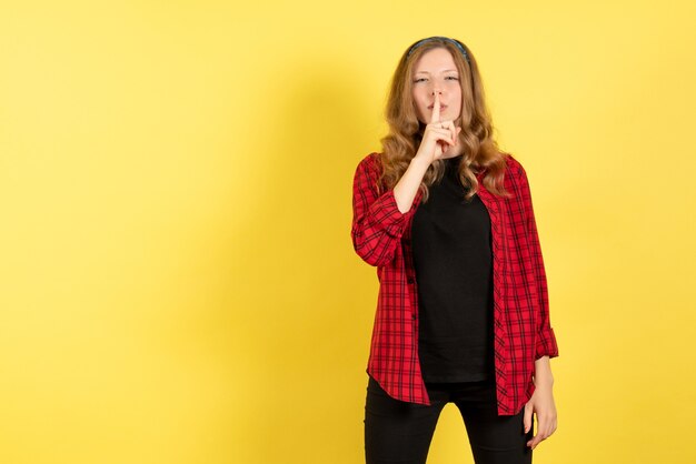 Vue de face jeune femme en chemise à carreaux rouge demandant d'être calme sur fond jaune fille humaine modèle couleur émotion femme