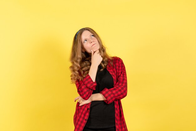 Vue de face jeune femme en chemise à carreaux rouge posant et pensant sur fond jaune femme modèle d'émotion humaine fille de mode