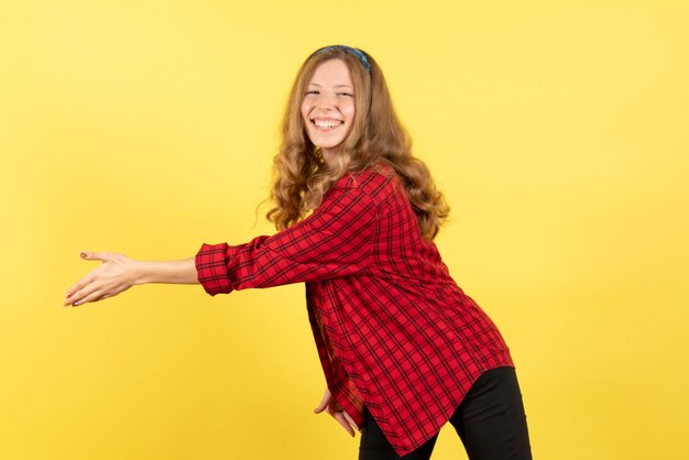 Vue de face jeune femme en chemise à carreaux rouge souriant et saluant quelqu'un sur fond jaune femme modèle d'émotion humaine fille de mode