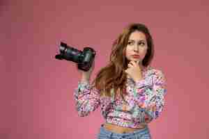 Photo gratuite vue de face jeune femme en chemise conçue de fleurs et blue-jeans pensant et tenant un appareil photo sur le fond rose