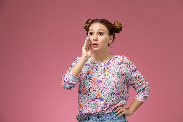 Vue de face jeune femme en chemise conçue de fleurs et blue jeans posant essayant de parler sur fond rose