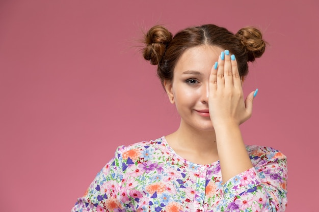 Vue de face jeune femme en chemise conçue de fleurs et blue-jeans souriant et couvrant son visage sur le fond rose