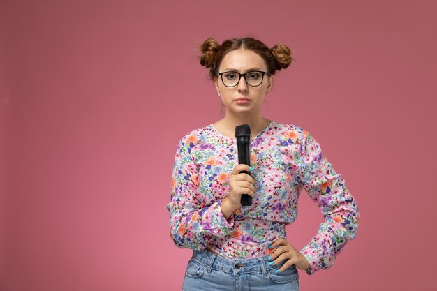 Vue de face jeune femme en chemise conçue de fleurs essayant de signer avec microphone le fond rose