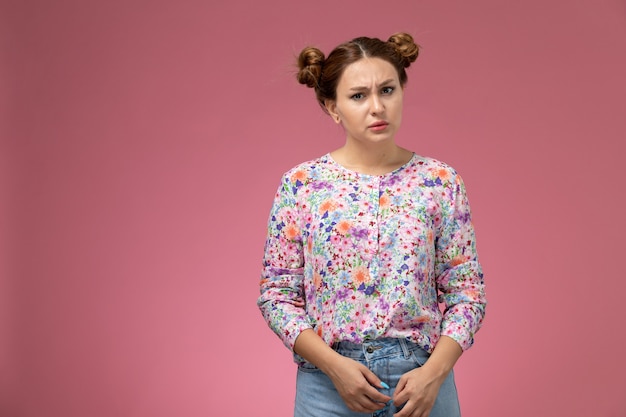 Vue de face jeune femme en chemise conçue de fleurs et jeans bleu posant juste sur le fond rose